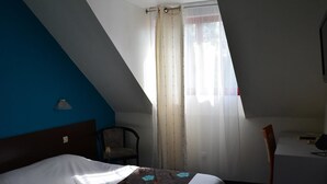 A hotel room with a bed, a desk, a chair, and a window with curtains. - Logis Hotel Lucotel (Lanvollon)