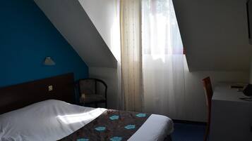 A hotel room with a bed, a desk, a chair, and a window with curtains.