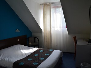 Ein Hotelzimmer mit einem Bett, einem Schreibtisch, einem Stuhl und einem Fenster mit Vorhängen.