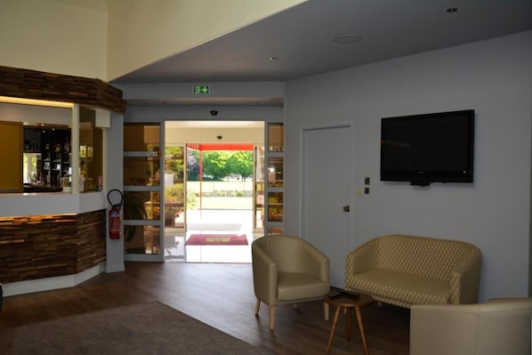 A reception area with a counter, a television mounted on the wall, and seating arrangements. - Hotel Lucotel (Lanvollon)