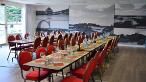A conference room with long tables set for a meeting, red chairs, and a scenic mural on the wall. - Logis Hotel Lucotel (Lanvollon)