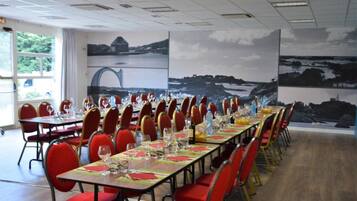 A conference room with long tables set for a meeting, red chairs, and a scenic mural on the wall.