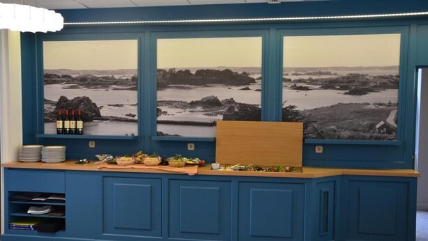 Una reception con un'ampia vetrata che mostra un paesaggio costiero, un portabottiglie per vino e un'area buffet.
