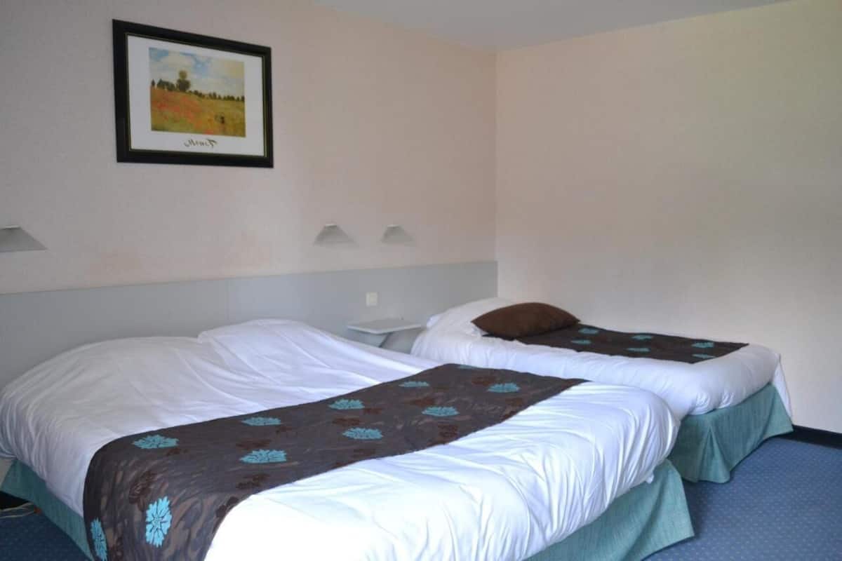 Two single beds with white linens and brown floral bedspreads, a framed landscape painting on the wall, and a small bedside table with a lamp.