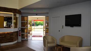 A lobby with a reception desk, a television mounted on the wall, and seating area with two chairs.
