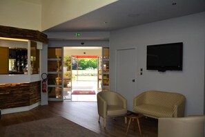 A lobby with a reception desk, a television mounted on the wall, and seating area with two chairs. - Logis Hotel Lucotel (Lanvollon)