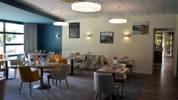 A restaurant with multiple tables and chairs, a chalkboard menu, and wall-mounted lights. - Logis Hotel Lucotel (Lanvollon)