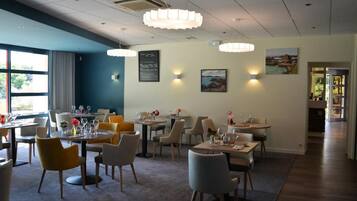 A restaurant with multiple tables and chairs, a chalkboard menu, and wall-mounted lights.