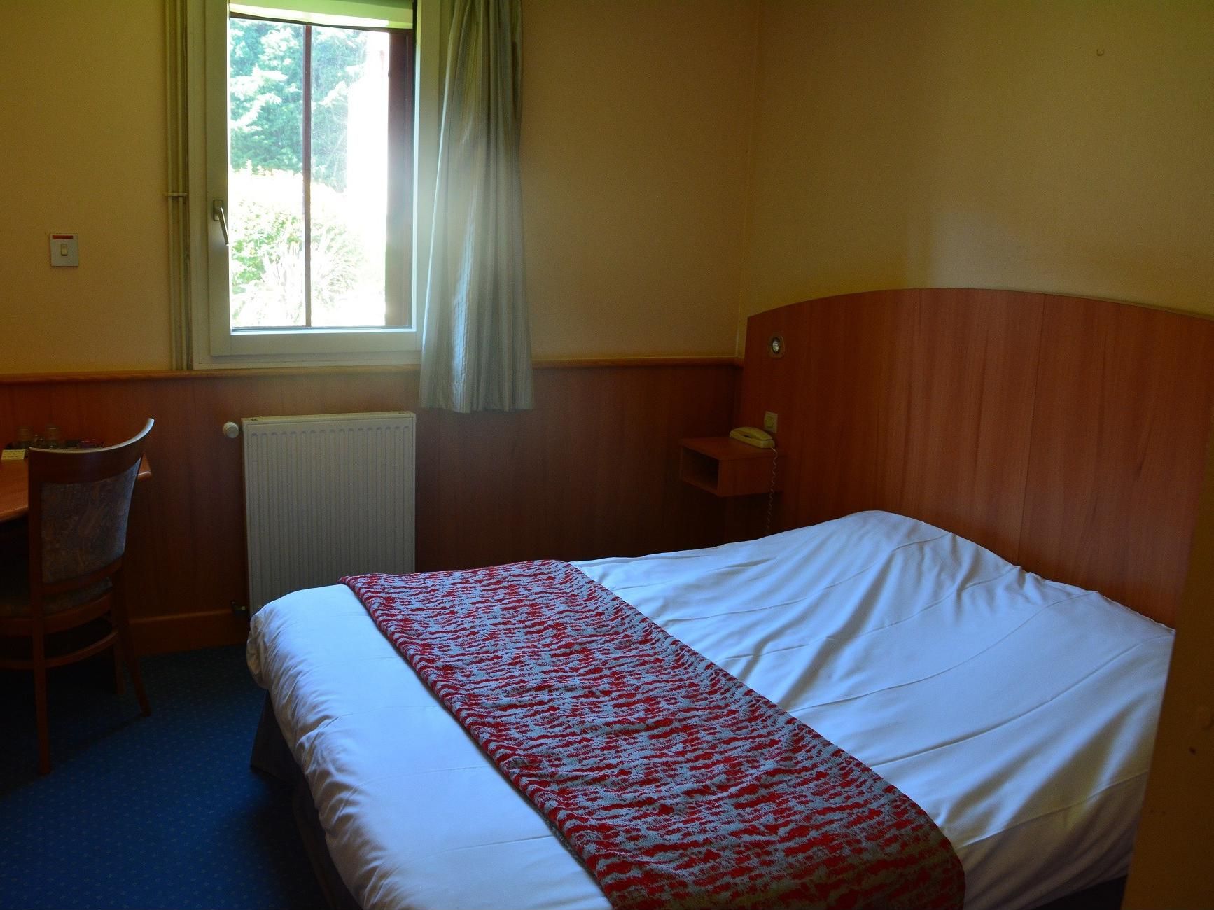 Een hotelkamer met een bed, bureau, stoel, telefoon en een raam met gordijnen.