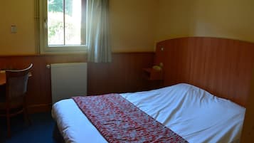 Een hotelkamer met een bed, bureau, stoel, telefoon en een raam met gordijnen.