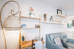 Una sala de estar moderna con un sofá azul, estanterías de madera, una lámpara colgante y un escritorio pequeño.