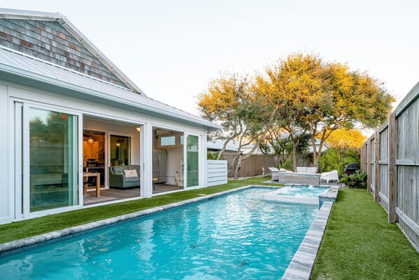 A modern house with a swimming pool, a covered patio, and a well-maintained lawn.