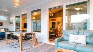 A modern living room with a blue sofa, a wooden dining table, and a glass door leading to a kitchen. - Family Tide Retreat/Heated Pool & 2 Spas (St. Augustine)
