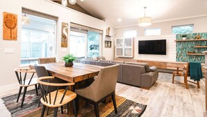 A spacious living room with a wooden dining table, comfortable seating, a large TV, and a view of the outdoors. - Family Tide Retreat/Heated Pool & 2 Spas (St. Augustine)