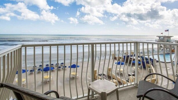 Un balcón con vista a la playa y al océano, con sillones y sombrillas.