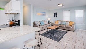 A modern living room with a kitchen area, featuring a large island, two sofas, and a coffee table.