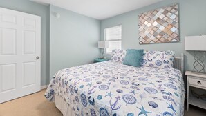 A bedroom with a bed, a nightstand, a wall-mounted lamp, and a door.