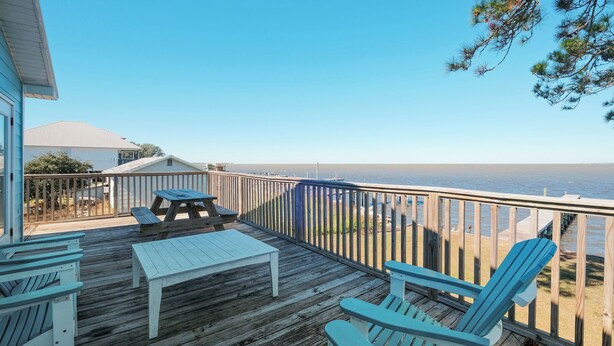 A wooden deck with Adirondack chairs and picnic tables overlooking a beach.