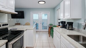 A kitchen with white cabinets, a black stove, a coffee maker, and a dining area with a chair and table.