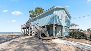 A two-story beach house with a wooden deck and stairs leading to the entrance.