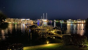 A marina at night with boats docked, a waterfront promenade, and buildings in the background. - Modern large 2 bedroom/2 bath Condo on Intercoastal with gorgeous  sunset views (St Pete Beach)