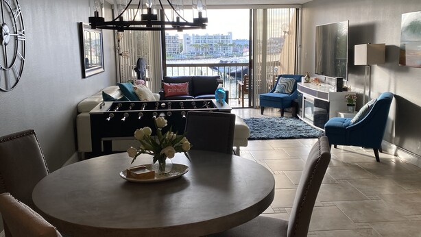 A modern living room with a round dining table, a sofa, a blue armchair, and a view of the beach through large windows. - Modern large 2 bedroom/2 bath Condo on Intercoastal with gorgeous  sunset views (St Pete Beach)