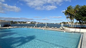 A swimming pool with lounge chairs and umbrellas, a view of the water, and a clear sky. - Modern large 2 bedroom/2 bath Condo on Intercoastal with gorgeous  sunset views (St Pete Beach)