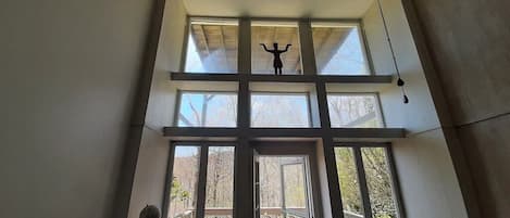 Enjoy a spacious room with a high ceiling and large windows offering a view of the outdoor deck area.