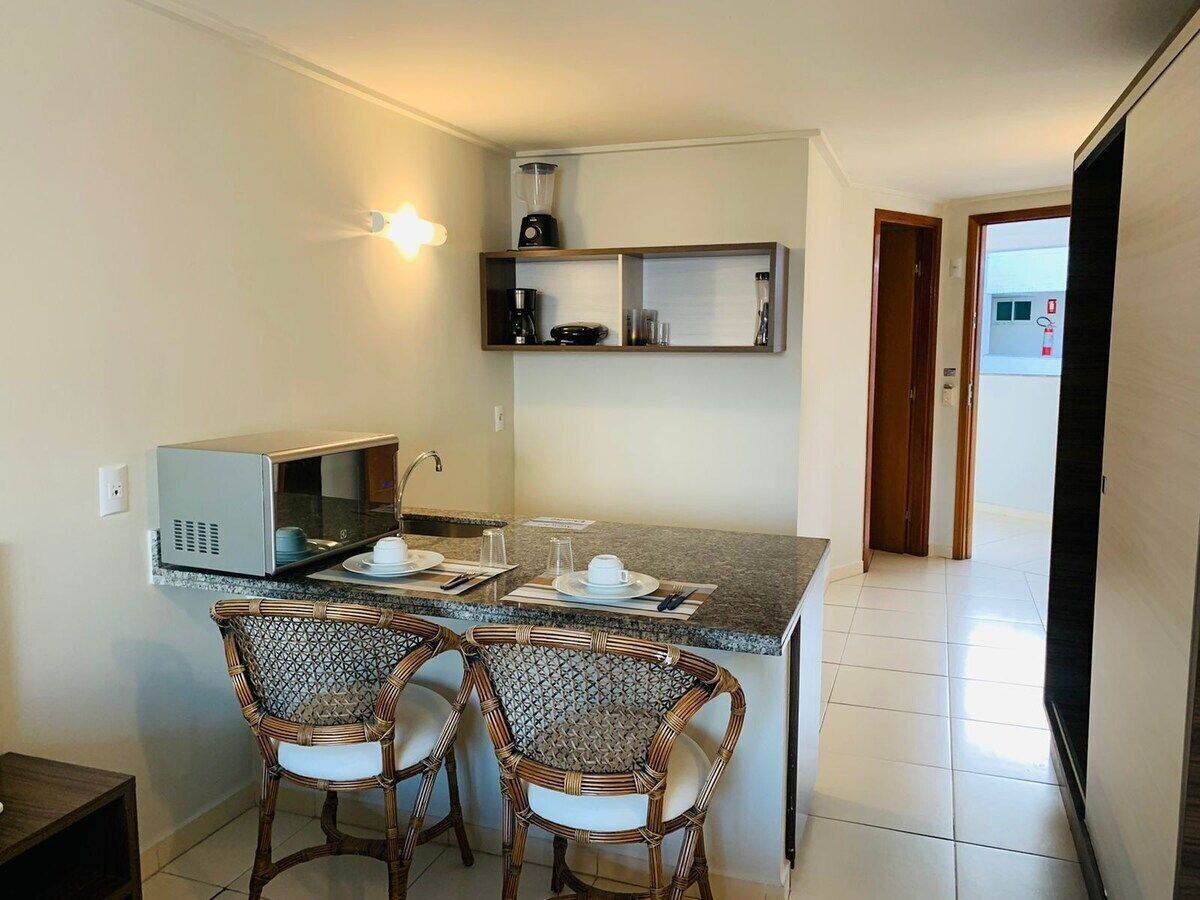 A compact kitchen with a microwave, coffee maker, and a blender on the countertop. There are two wicker chairs and a small dining table.