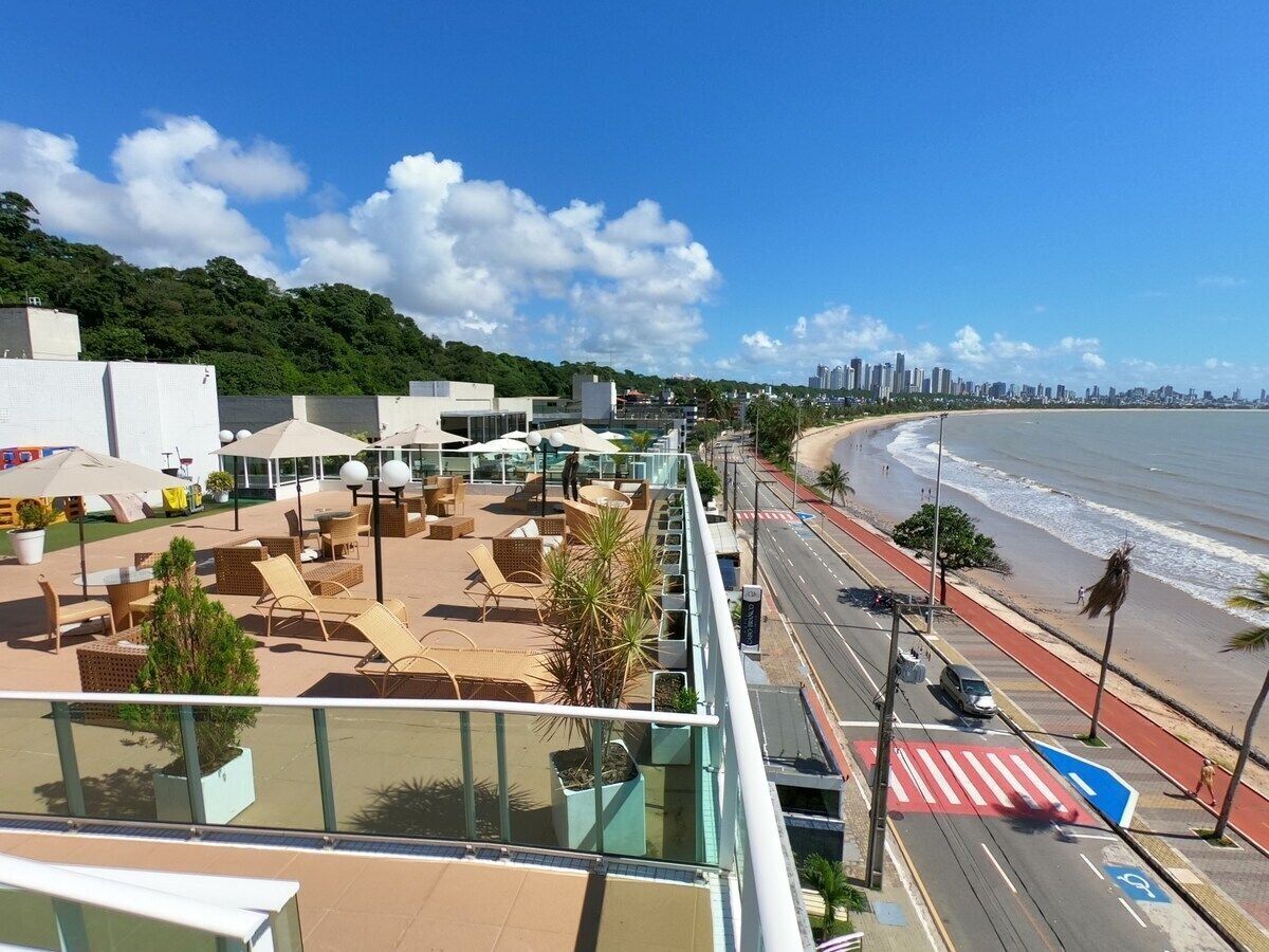 Une terrasse sur le toit avec des sièges extérieurs, une vue sur la plage et un panorama de la ville en arrière-plan.