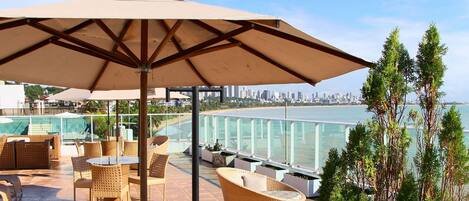 A rooftop terrace with outdoor seating, a large umbrella, and a view of the city skyline and water.