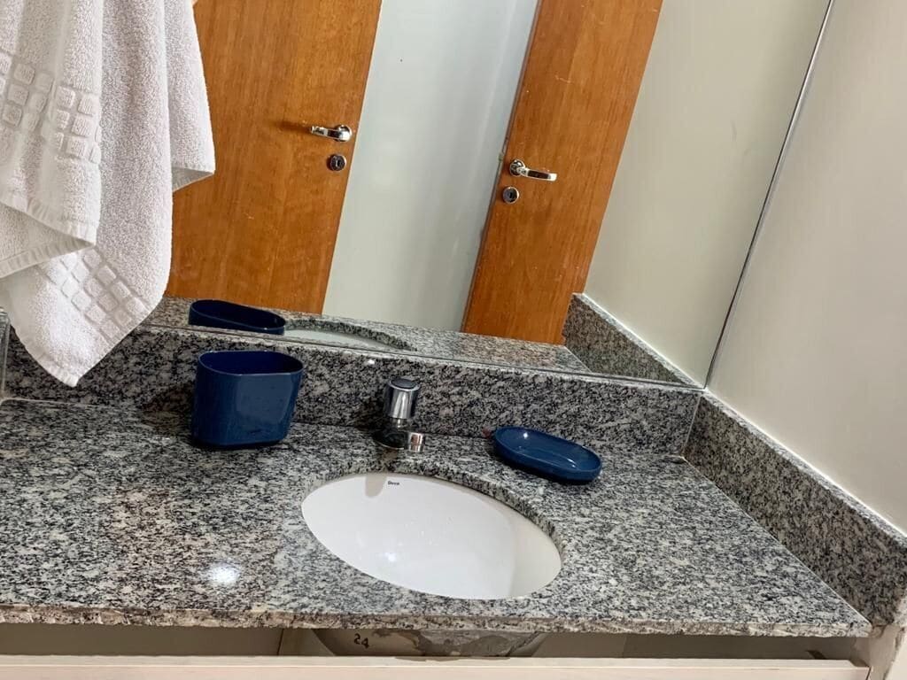 A bathroom with a granite countertop, a white sink, a blue soap dish, and a towel hanging on the wall.