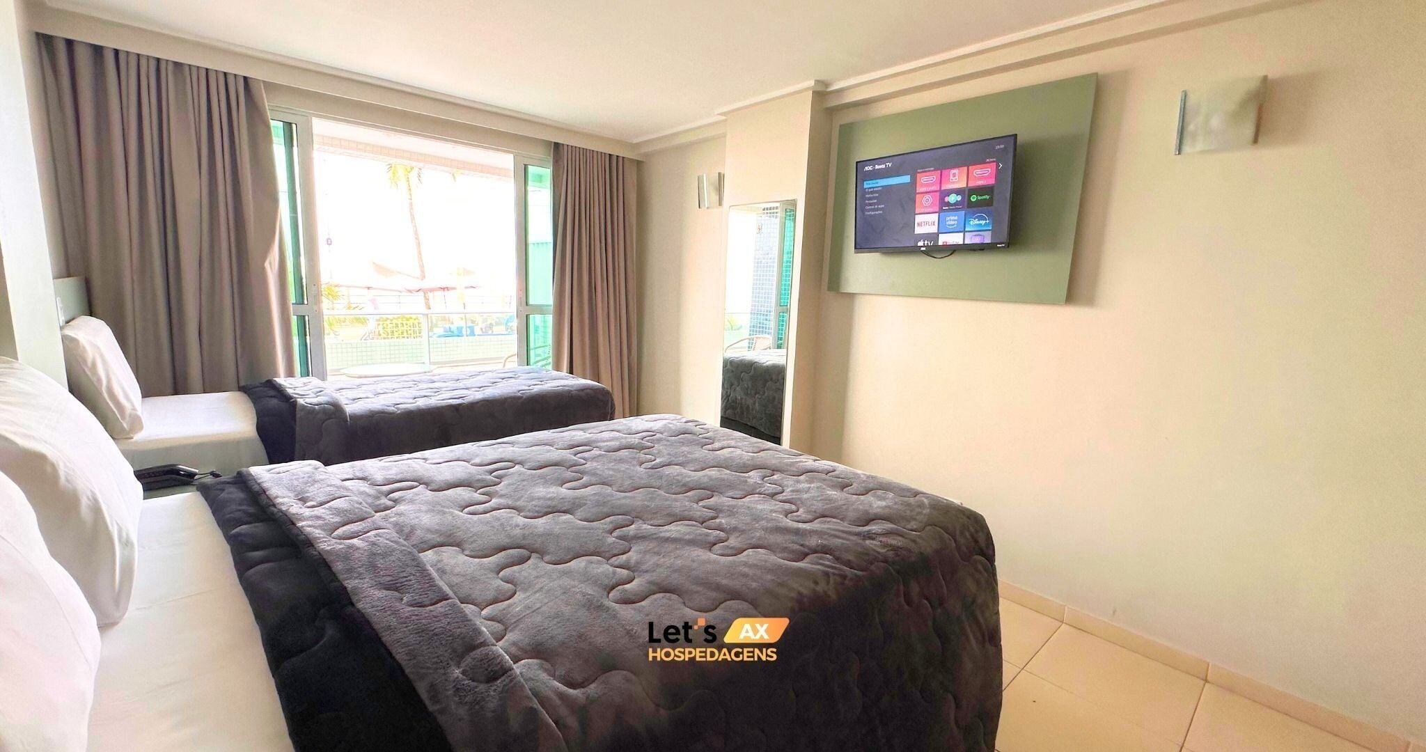 Habitación de hotel con dos camas, un televisor en la pared y una ventana con cortinas.