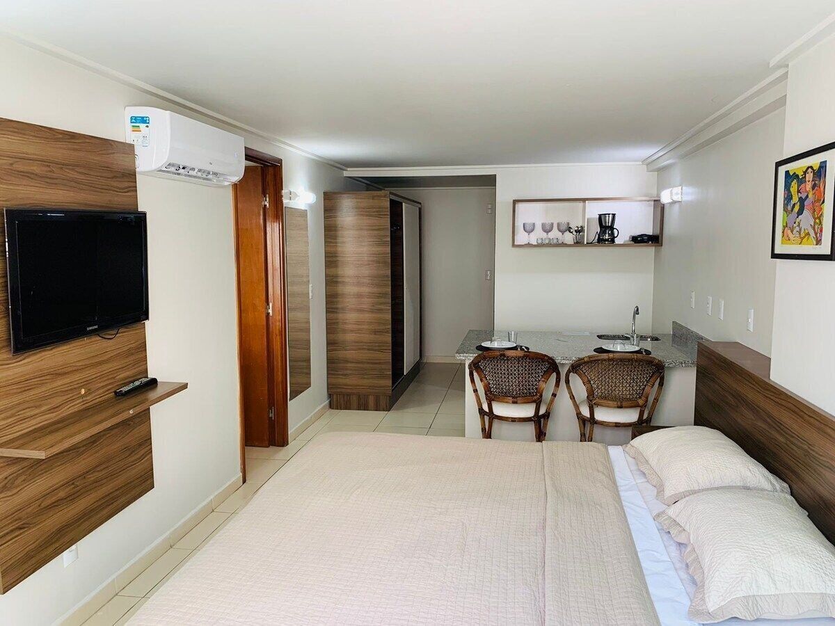 A hotel room with a bed, a TV, a desk with chairs, and a kitchenette.