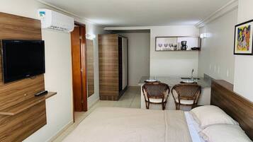 A hotel room with a bed, a TV, a desk with chairs, and a kitchenette.