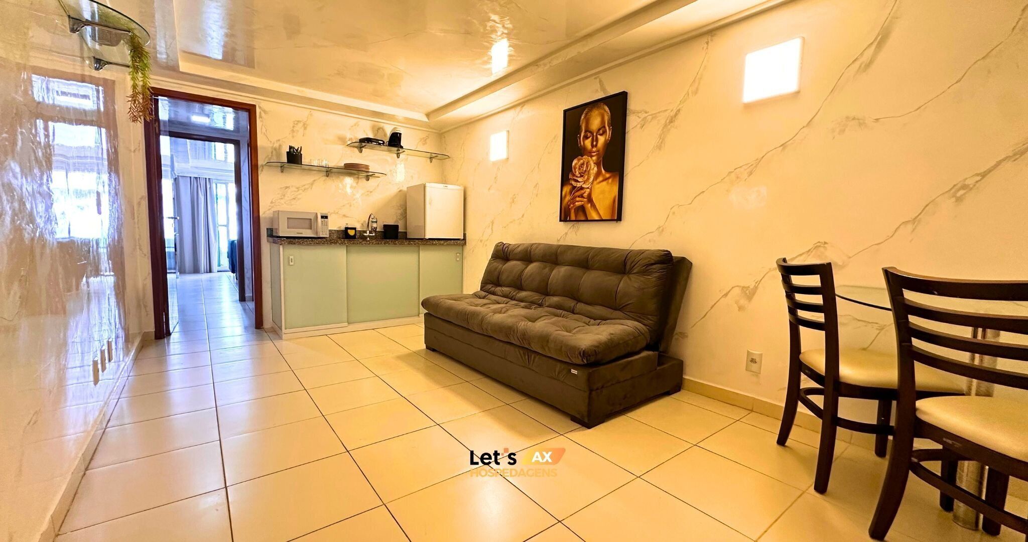 A living room with a sofa, a dining table with chairs, a kitchen area with a microwave, and a painting on the wall.