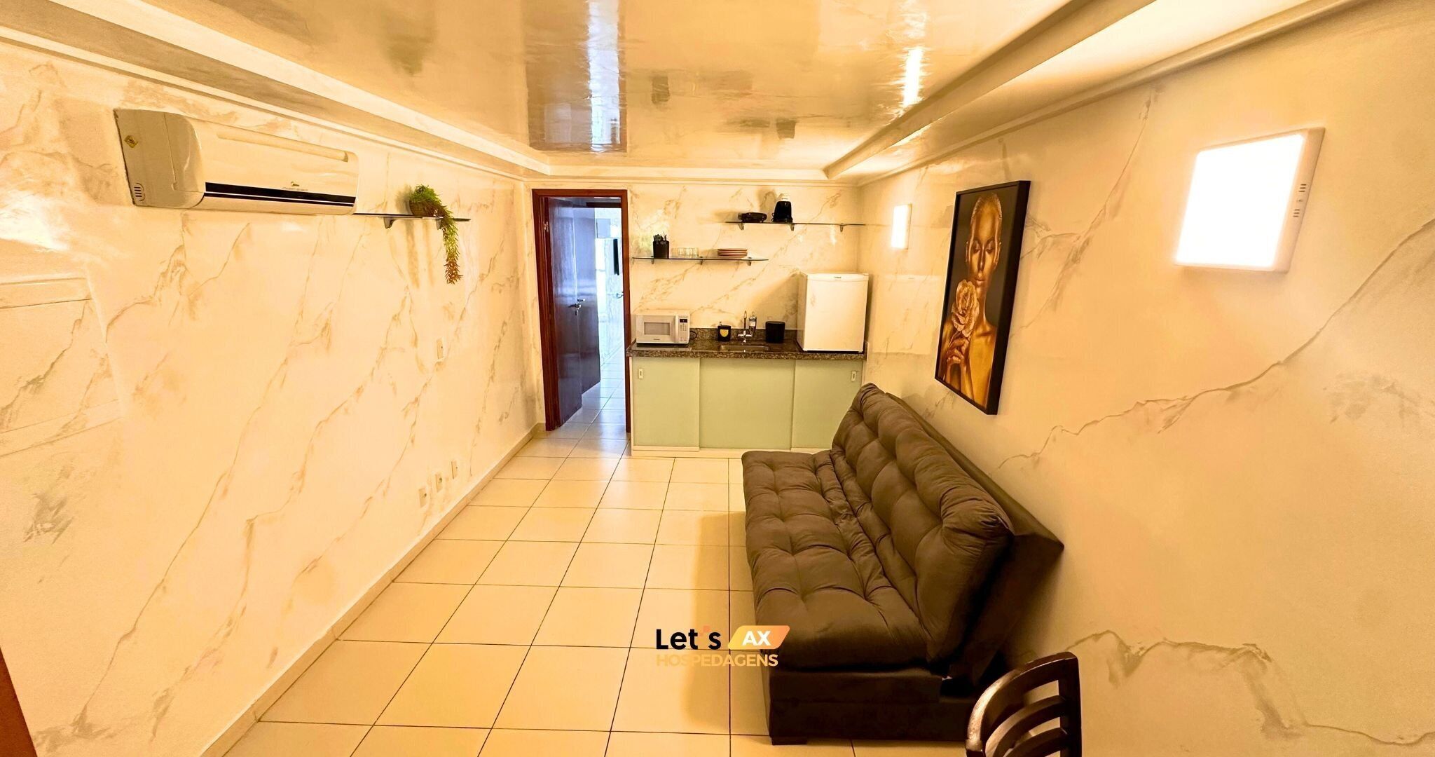 A hallway with a marble wall, a sofa, a chair, a kitchen area, and a door leading to another room.