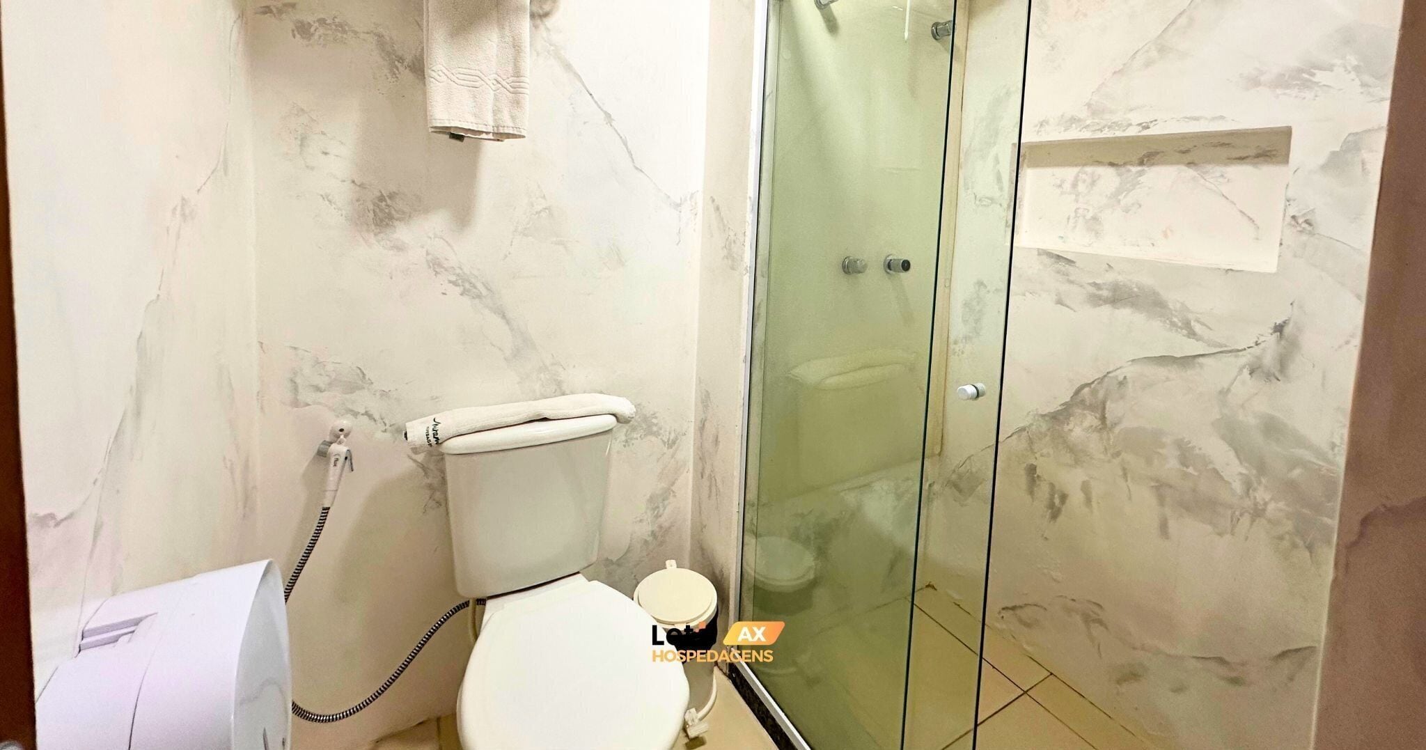 A bathroom with a toilet, a glass shower enclosure, and a marble wall.