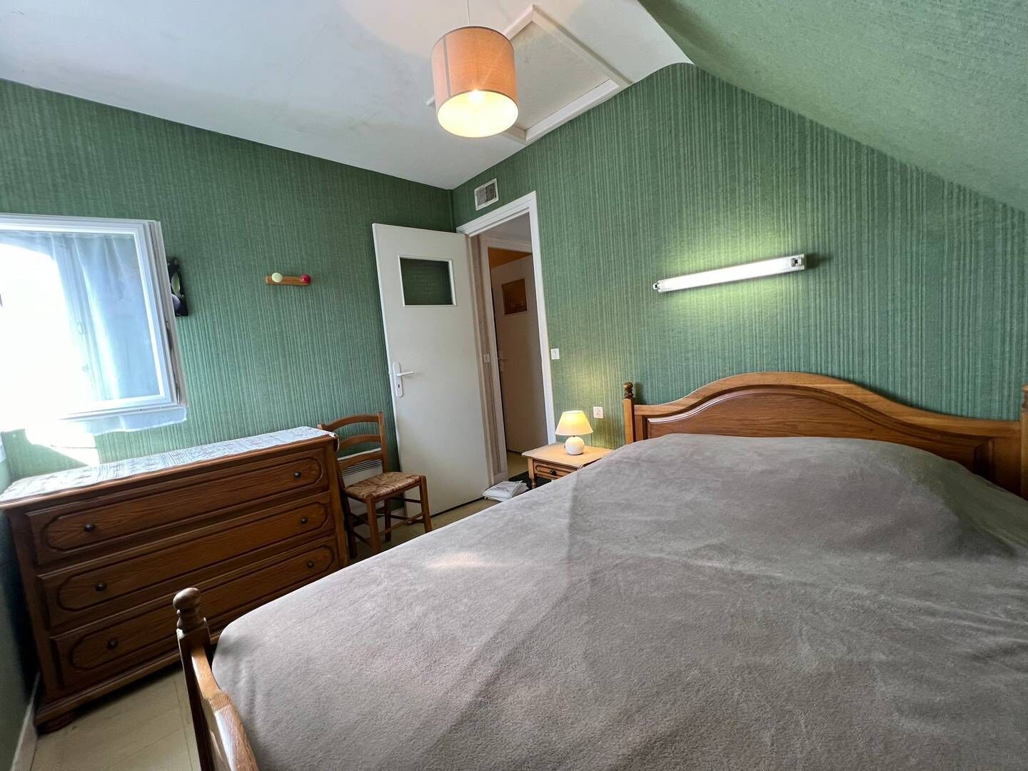 A bedroom with a bed, dresser, chair, and a door leading to another room.