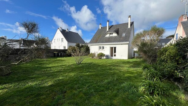 A white house with a sloped roof, a small garden, and a clear blue sky.