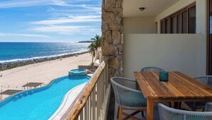 Een balkon met uitzicht op strand en zee, een houten tafel en rieten stoelen.