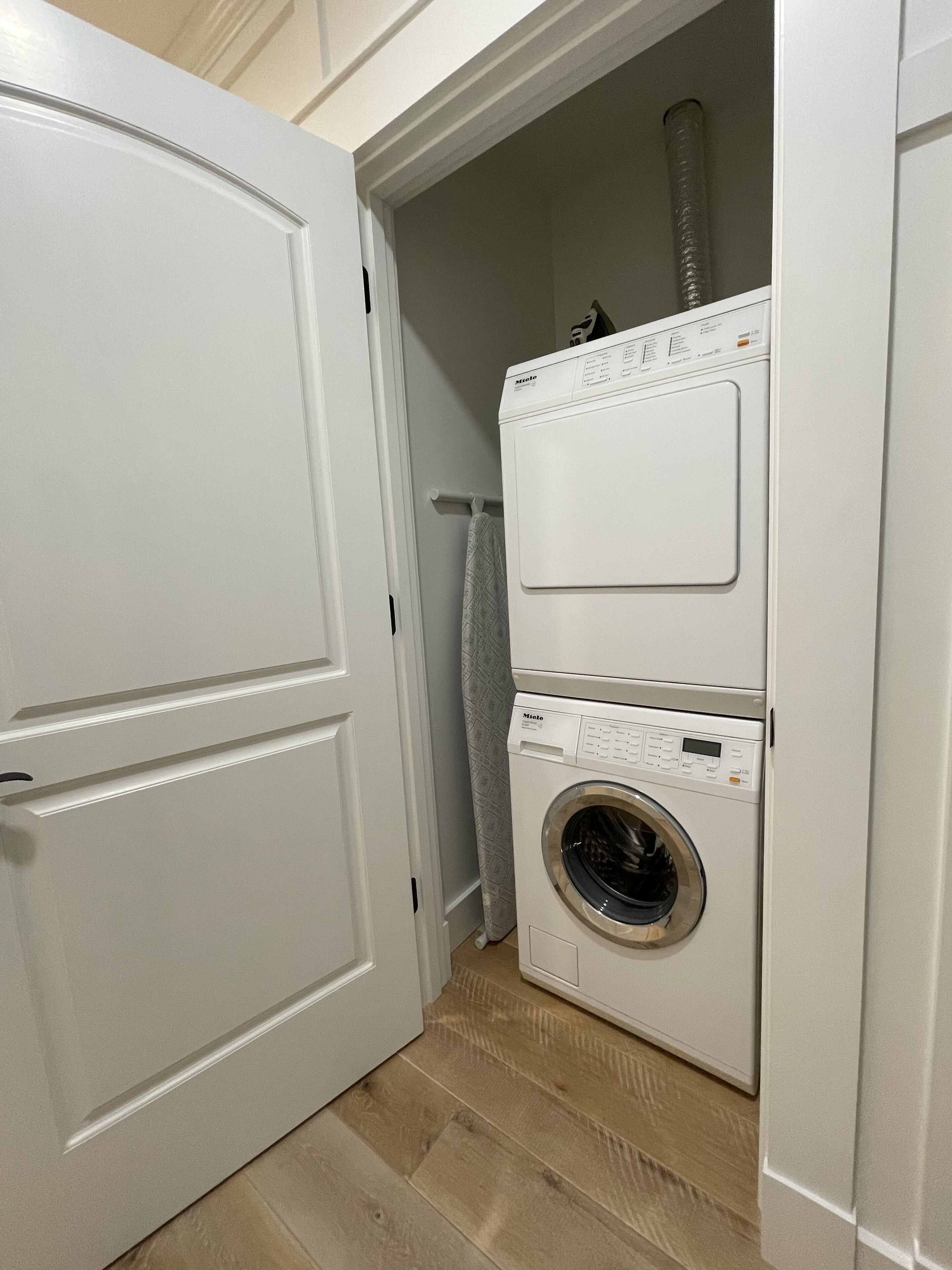 Un cuarto de lavandería con lavadora y secadora de carga frontal, un perchero y una puerta que da a otra habitación.