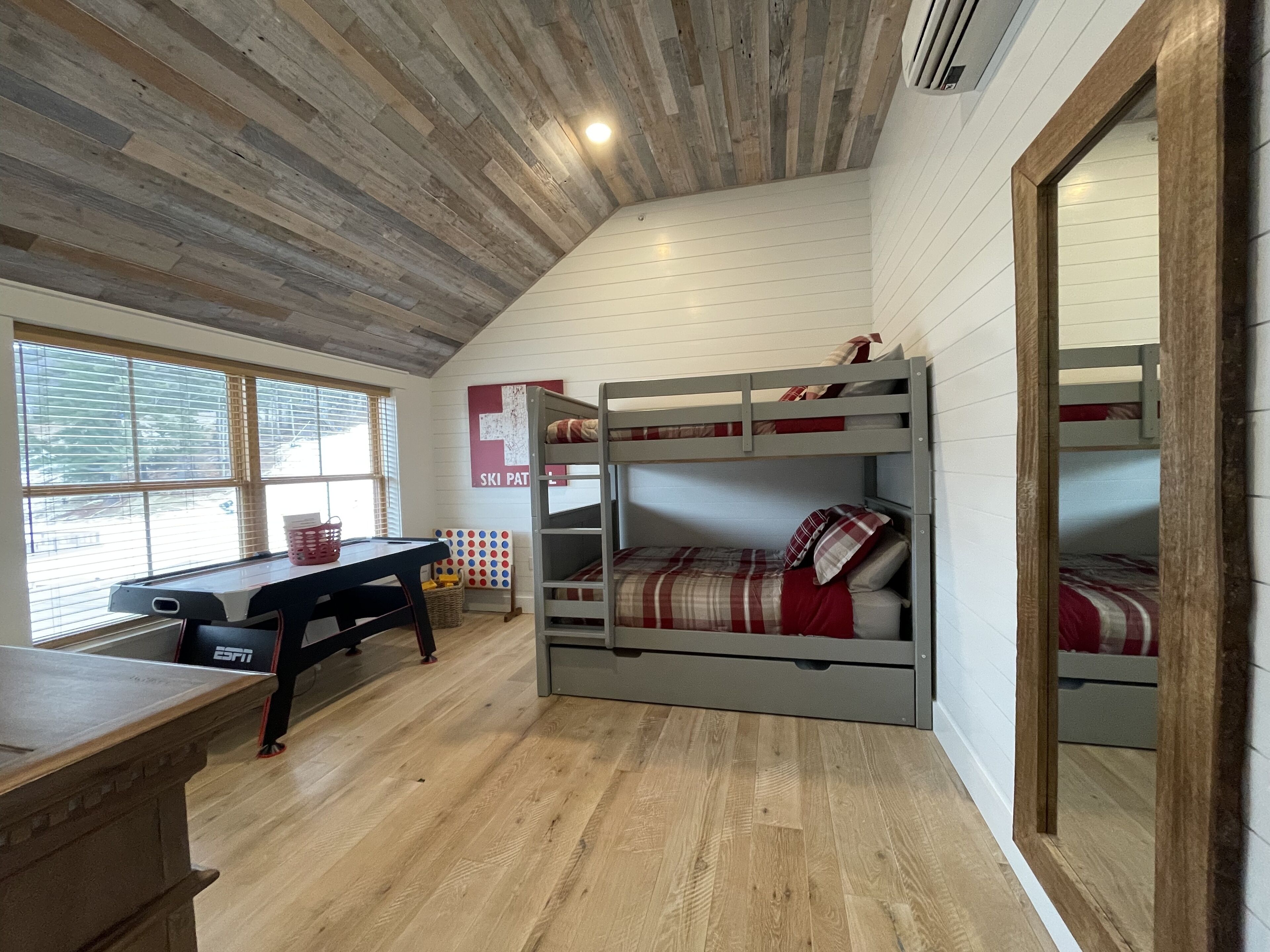 Une chambre avec des lits superposés, un bureau en bois et une fenêtre avec des stores.