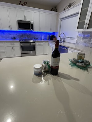 A modern kitchen with white cabinets, a stainless steel oven, a microwave, and a blue-lit backsplash. - Coastal Beach Home in the heart of Key Largo. (Key Largo)