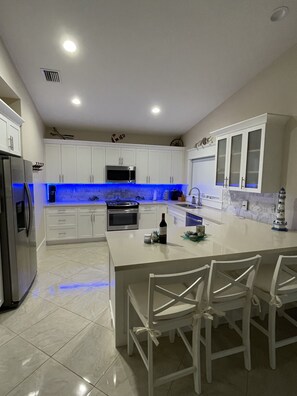 A modern kitchen with white cabinets, a central island with chairs, a microwave, oven, and a refrigerator. - Coastal Beach Home in the heart of Key Largo. (Key Largo)