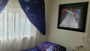 Un dormitori amb un llit, una finestra amb cortines lleugeres i un quadre al mur.