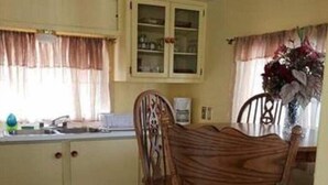 Una cuina amb armaris de fusta, una taula de dinar amb cadires i una finestra amb cortines.