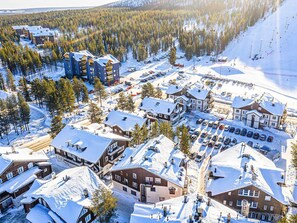 A snow-covered town with multiple buildings, including a hotel with a ski lift visible in the background.