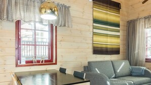 Ein gemütlicher Raum mit Holzvertäfelung, einer Couch, einem Esstisch mit Stühlen und einem Fenster mit Jalousien sowie einer dekorativen Hirschfigur.