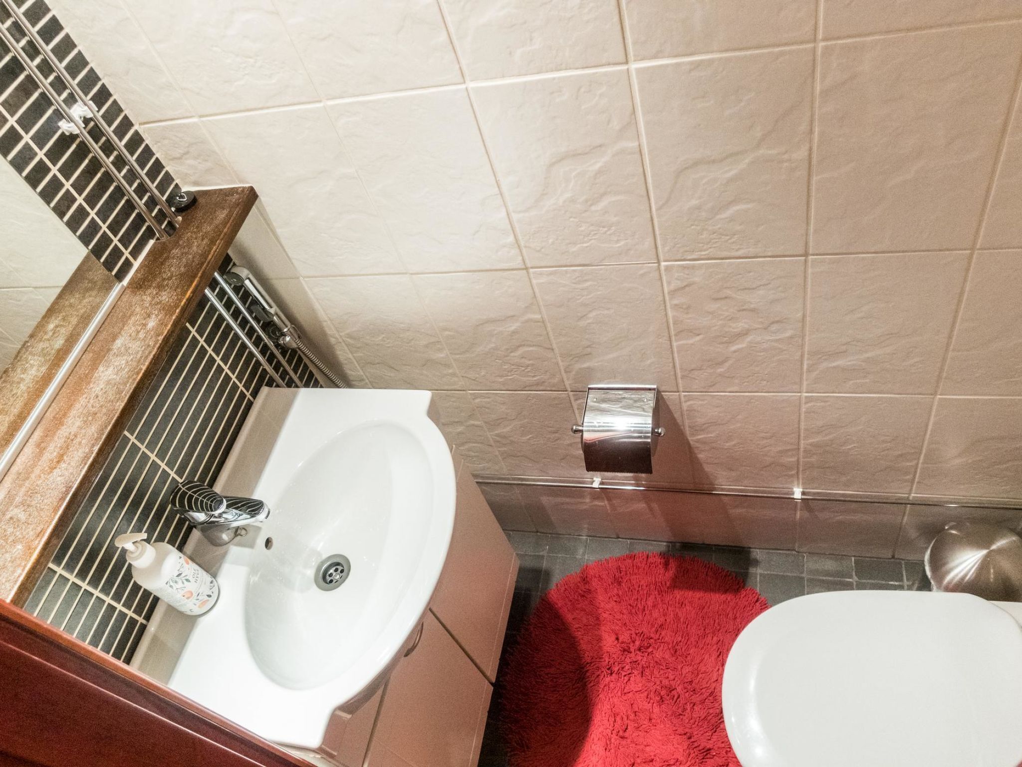 Une salle de bain avec un lavabo, des toilettes et un tapis rouge.
